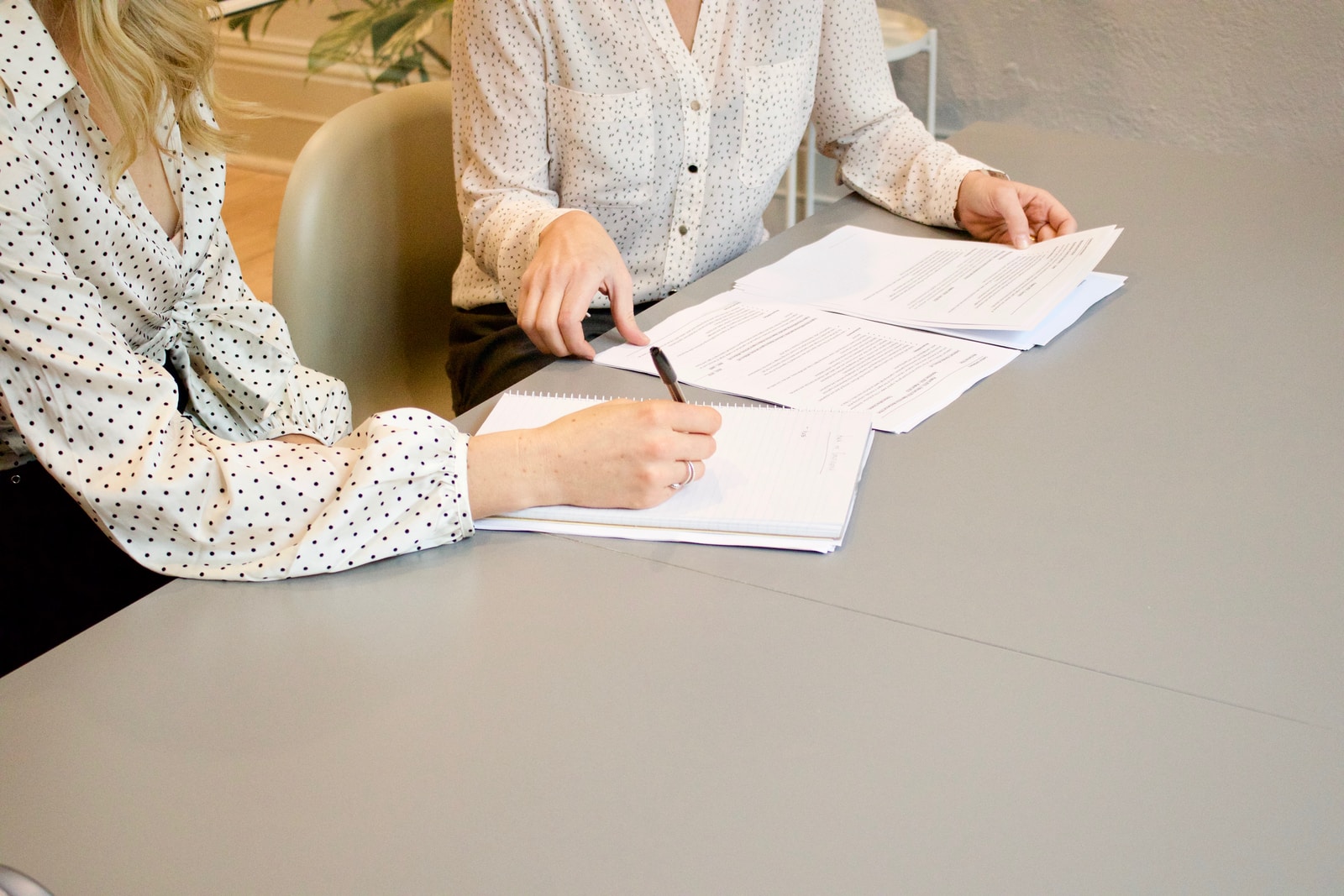 Home woman signing on white printer paper beside woman about to touch the documents